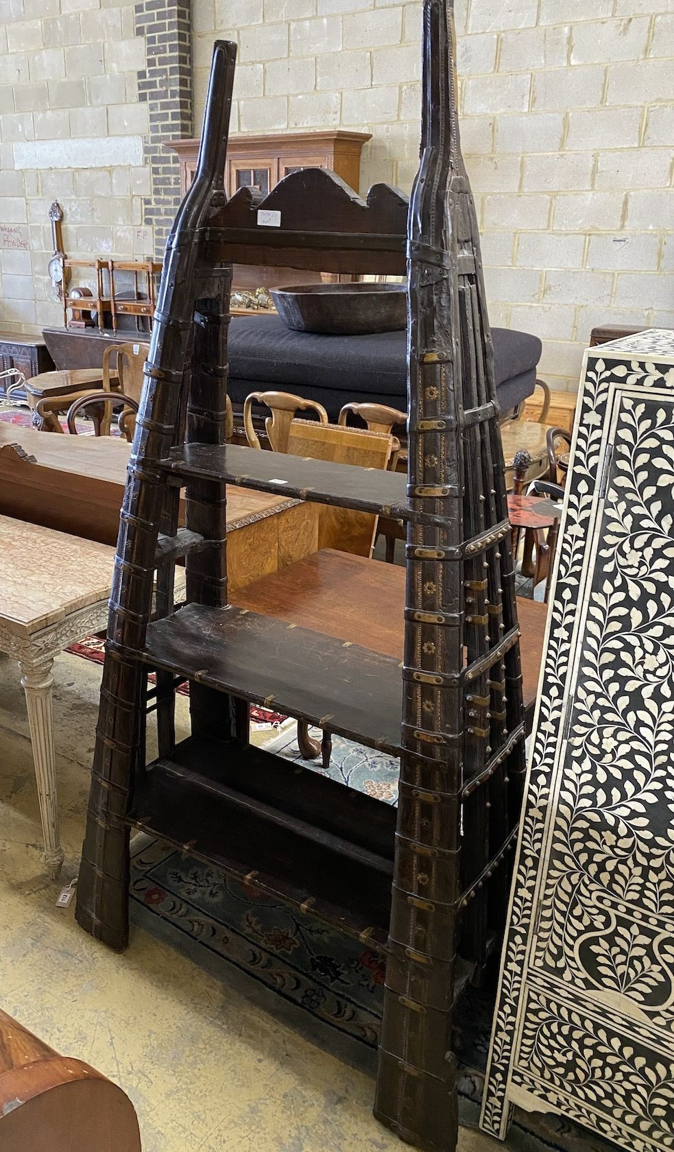 An Indian brass mounted carved hardwood three tier shelf unit, constructed from a 19th century ox harness, length 106cm, depth 40cm, height 202cm